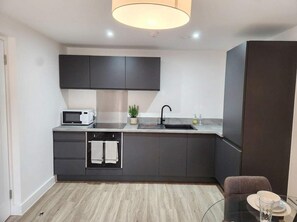 Une cuisine moderne avec des meubles de couleur sombre, un four à micro-ondes, un évier et un coin repas comprenant une table et des chaises en verre.