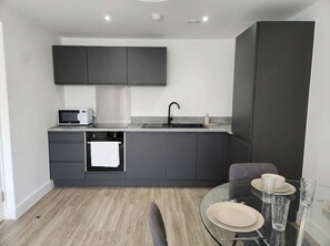 A modern kitchen with dark cabinetry, a microwave, a sink, and a dining area with a glass table and chairs.