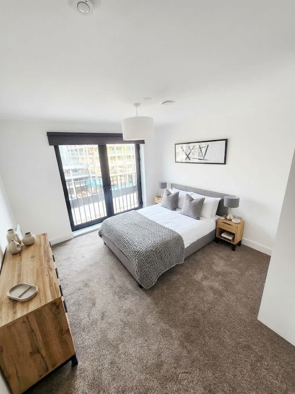 A bedroom with a bed, bedside tables, a wooden dresser, a large window, and a ceiling light.