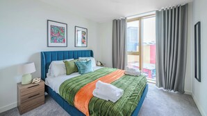 Une chambre d’hôtel avec un grand lit, une table de chevet avec une lampe, deux tableaux encadrés au mur et une vue sur la ville par la fenêtre.