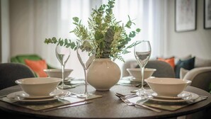 Une table à manger dressée avec des bols blancs, des verres à vin et un vase contenant des feuilles vertes.