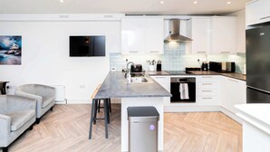A modern kitchen with a central island, white cabinetry, a built-in oven, and a stainless steel refrigerator. - Stylish 2BR Stay in Tonbridge Town Centre (Tonbridge)