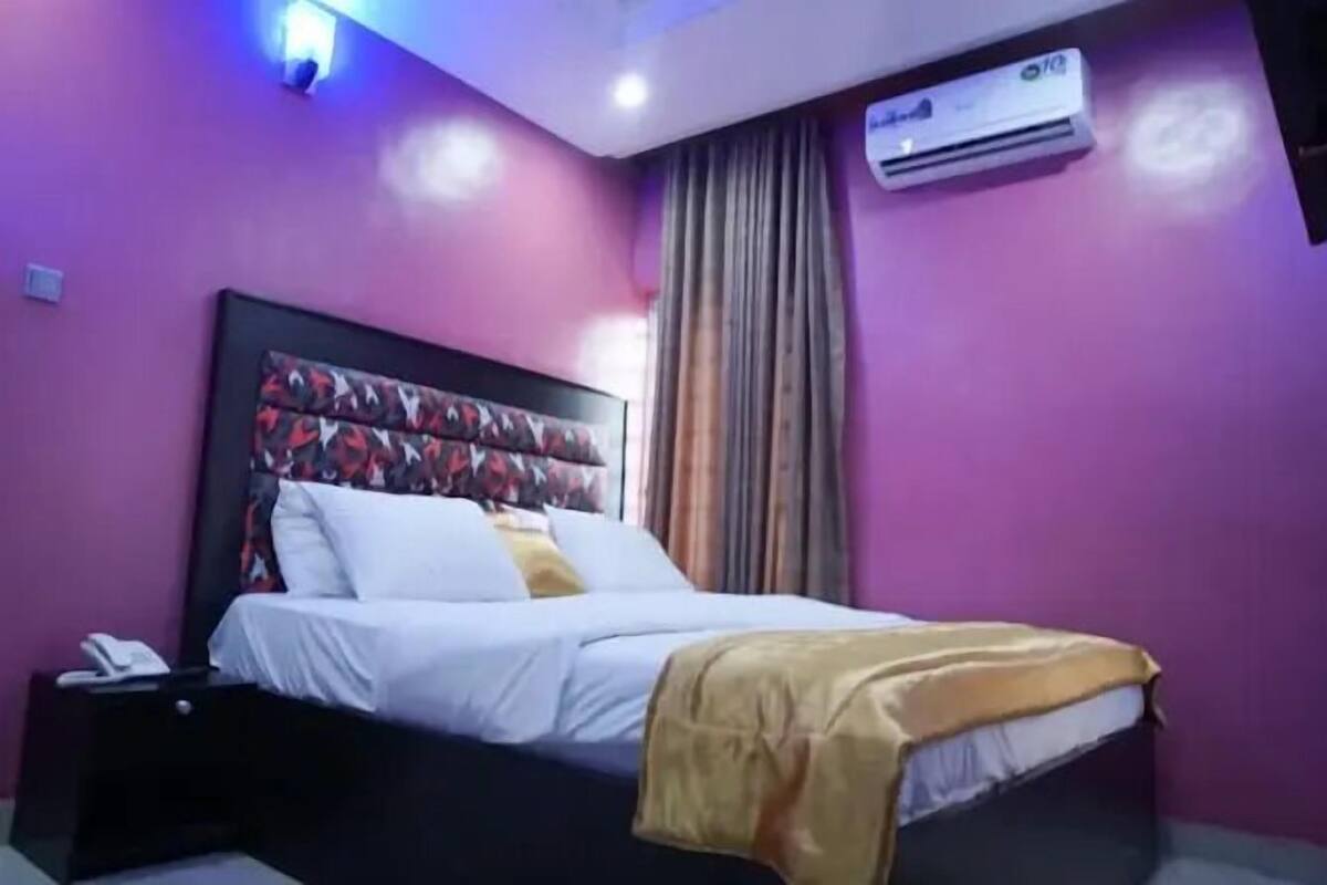 A bedroom with a bed, a nightstand, an air conditioner, and a window with curtains.