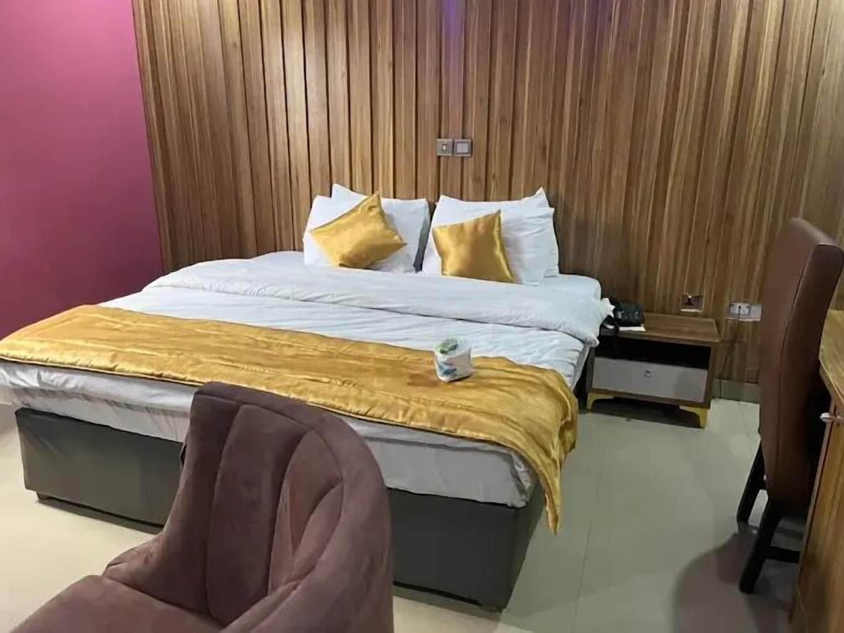 Habitación de hotel con cama, mesita de noche, una silla y pared de madera.