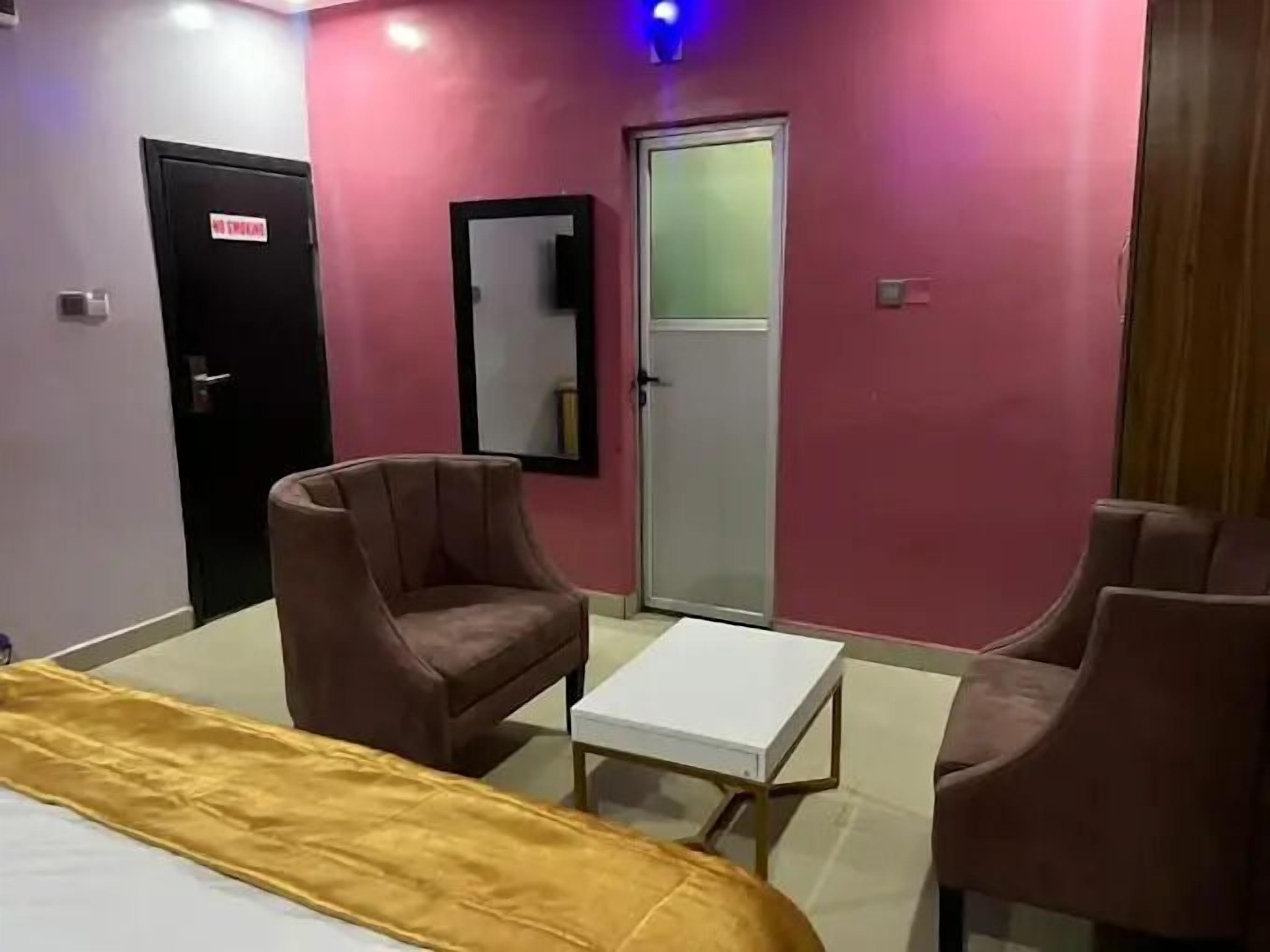 A hotel room with a bed, two armchairs, a small table, and a door marked "No Entry".