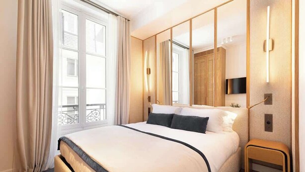 Une chambre d’hôtel moderne avec un grand lit, une petite table de chevet, un miroir et une vue sur le balcon extérieur.