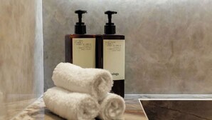 Une salle de bain avec deux flacons de lotion pour le corps et une serviette enroulée sur un comptoir en marbre.