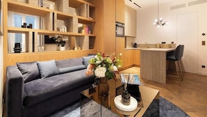 Un salon moderne avec un canapé, une table basse et un vase décoratif. On aperçoit à l’arrière-plan un coin cuisine avec une table à manger et des chaises.