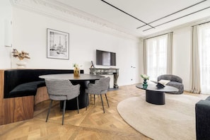 A modern living room with a black sofa, a dining table with chairs, a fireplace, and a TV mounted on the wall.