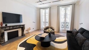 A modern living room with a fireplace, a flat-screen TV, a round coffee table with a book, a sofa, and a patterned rug. - ONIRI - Serviced 2-BR/2BA - Louvre Richelieu II (Paris)