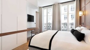 A modern hotel room with a large bed, a desk, and a TV mounted on the wall. - ONIRI - Serviced 2-BR/2BA - Louvre Richelieu II (Paris)