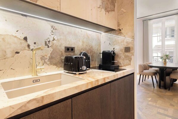 A modern kitchen with a marble countertop, a gold faucet, a black coffee maker, and a toaster.