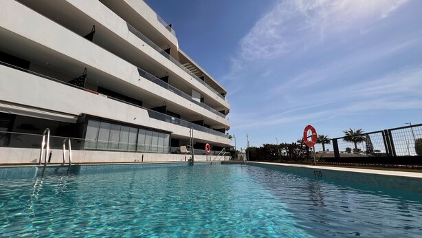 A modern building with a swimming pool, multiple balconies, and a clear sky. - 2 bedroom apartment in torrox costa (Torrox Costa)