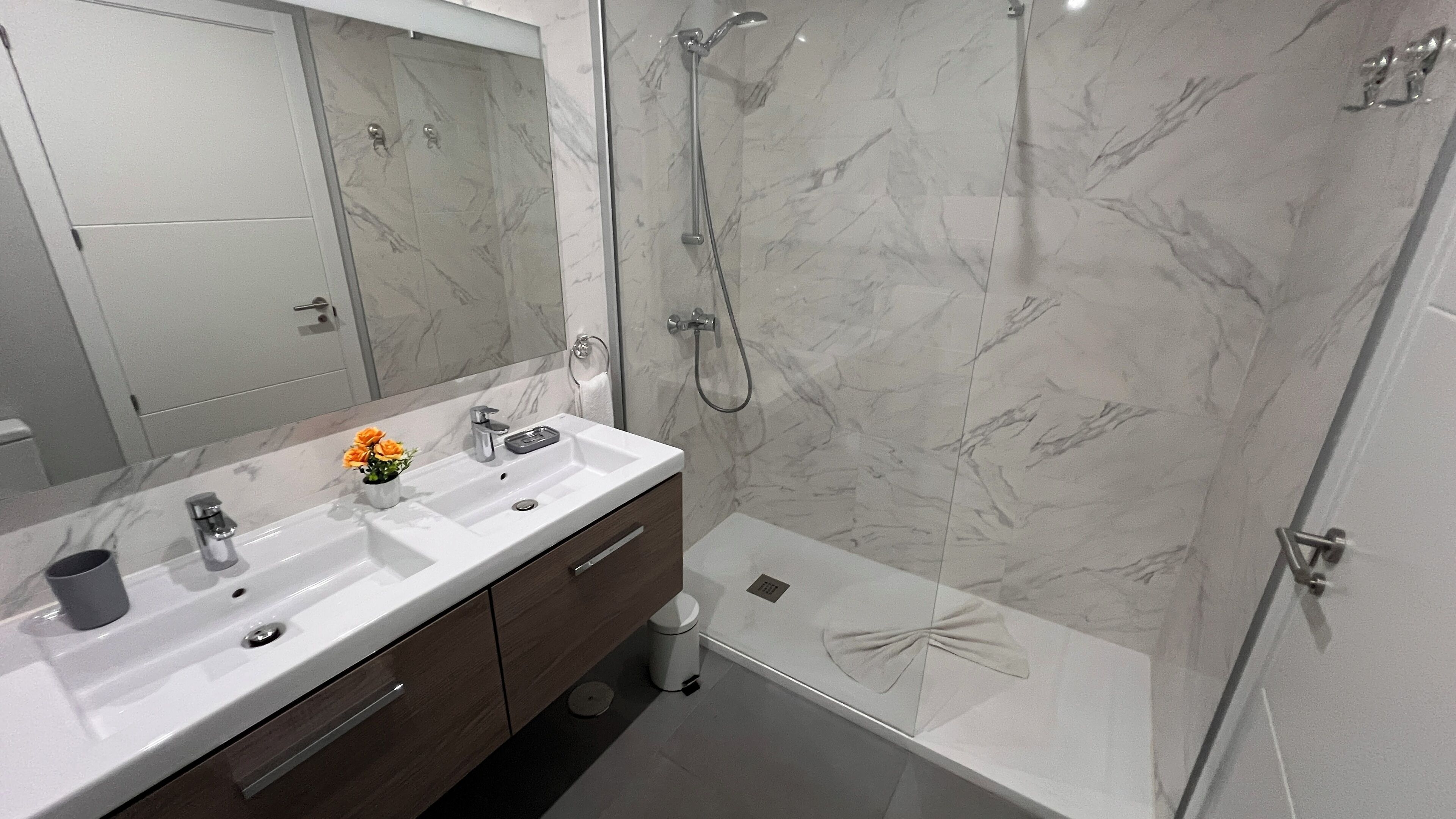 A modern bathroom with a marble shower, a double sink vanity, and a toilet.