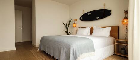 A bedroom with a bed, a surfboard on the wall, a plant, and a nightstand with a lamp.