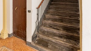 Una escalera con barandilla de madera y pasamanos de metal, que lleva a una puerta con un ventanal encima.