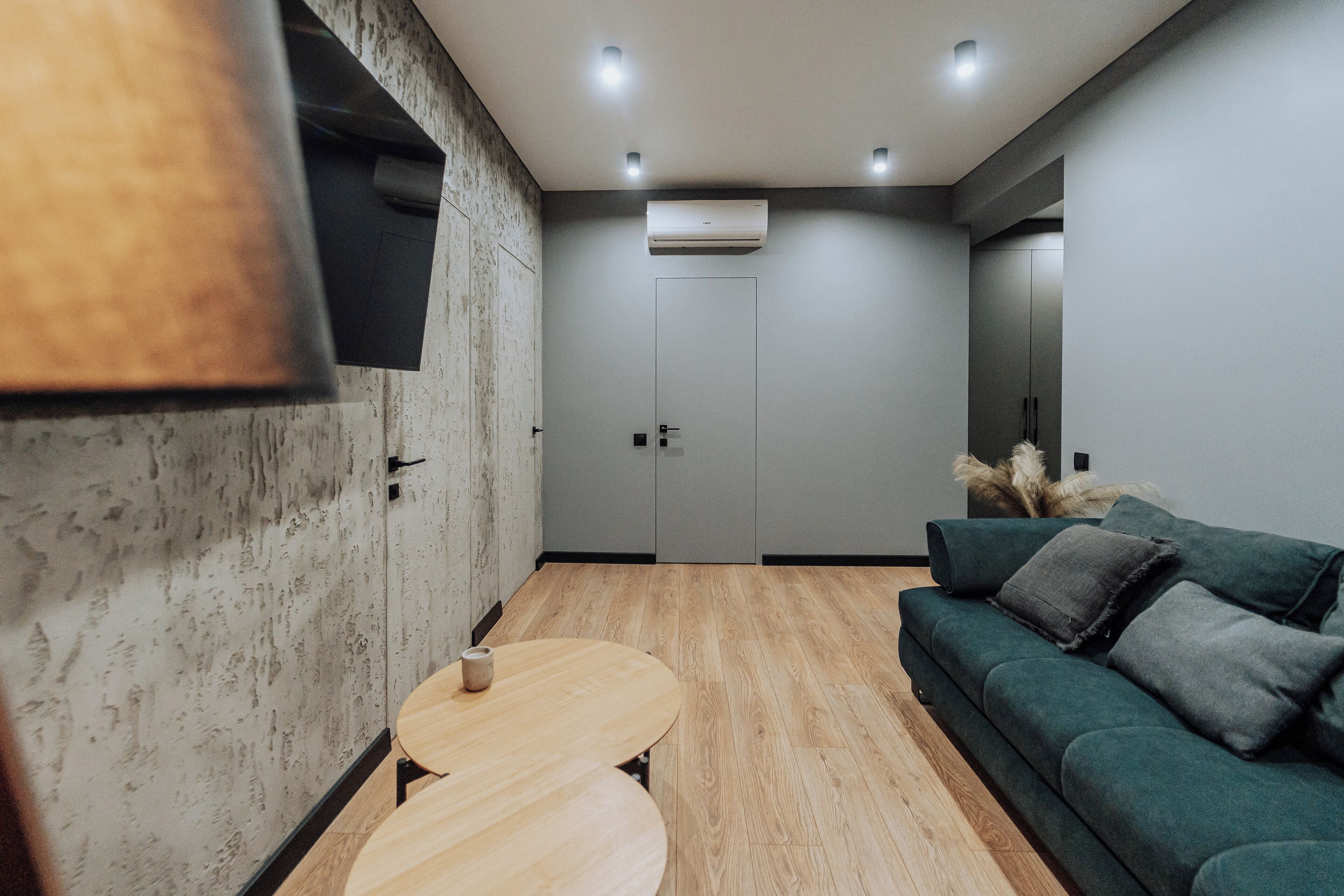 Une pièce moderne avec un plancher en bois, un canapé vert, une petite table ronde et une porte.