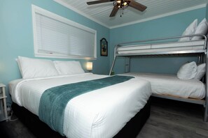 Una habitación con una cama individual, una litera, un ventilador de techo, una ventana con persianas y un reloj de pared.