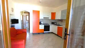 Eine moderne Küche mit weißen und orangefarbenen Schränken, eine Essecke mit einem roten Sofa und ein Fliesenboden.