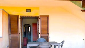 Ein überdachter Patio-Bereich mit Tisch und Stühlen, Holzläden und ein gefliestem Boden.