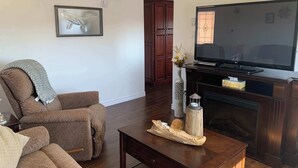 A living room with a sofa, a coffee table, a TV, and a fireplace. - Salty B'y Cottage (Twillingate)