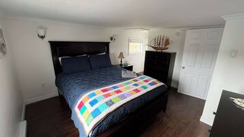 Een slaapkamer met een donker houten bed, een kleurrijke quilt, een nachtkastje met een lamp, een dressoir en een deur.