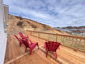 A wooden deck with red chairs and a railing overlooking a coastal landscape. - Salty B'y Cottage (Twillingate)