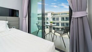A modern hotel room with a large bed, a balcony with a table and chairs, and a view of the building's exterior. - Naiharan Apartment UTN D604 near Beach (Rawai)