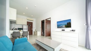 A modern living room with a blue sofa, a coffee table, and a TV on a white cabinet. - Naiharan Apartment UTN D604 near Beach (Rawai)