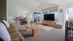 Uma sala de estar ampla com uma televisão grande, uma mesa de centro de madeira e um sofá.