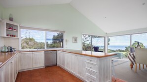 Uma cozinha com uma janela grande, vista para o exterior e um espaço de jantar com mesa e cadeiras.