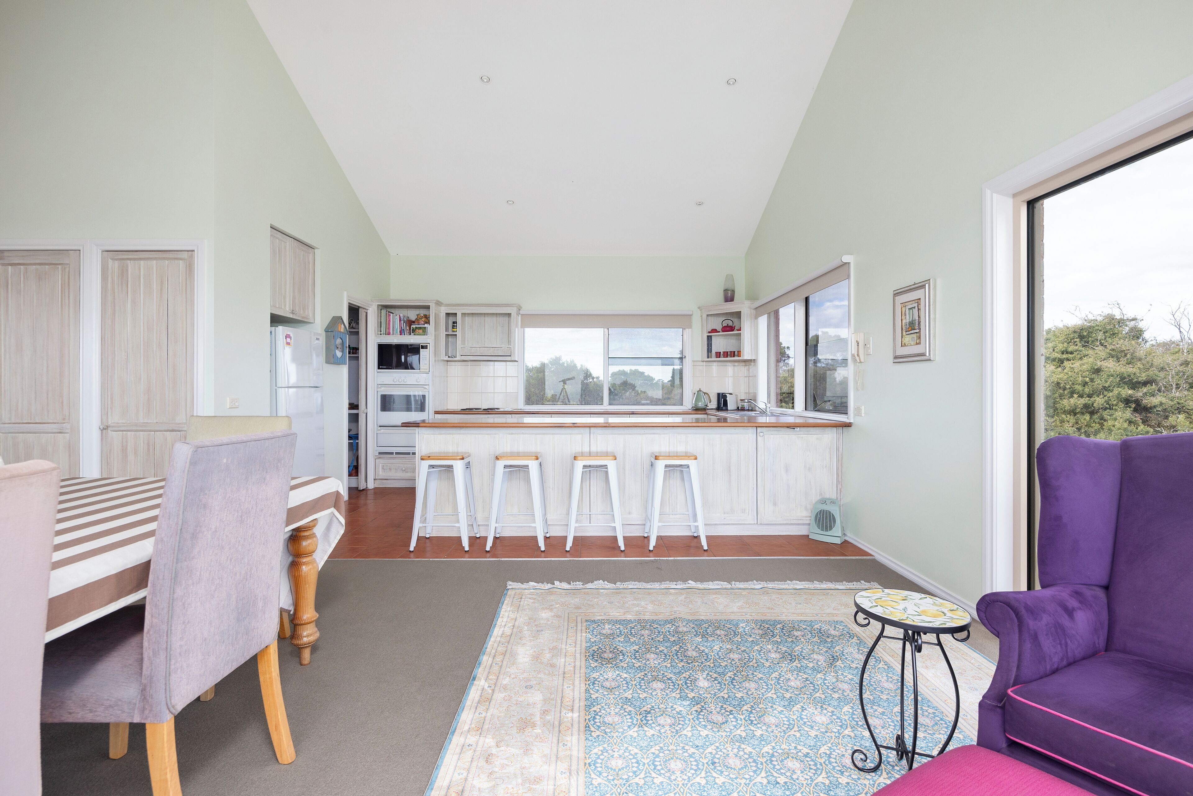 A modern kitchen with a central island, bar stools, and a dining table with chairs.