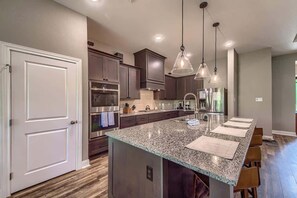 Una cocina moderna con encimeras de granito, electrodomésticos de acero inoxidable e iluminación colgante.