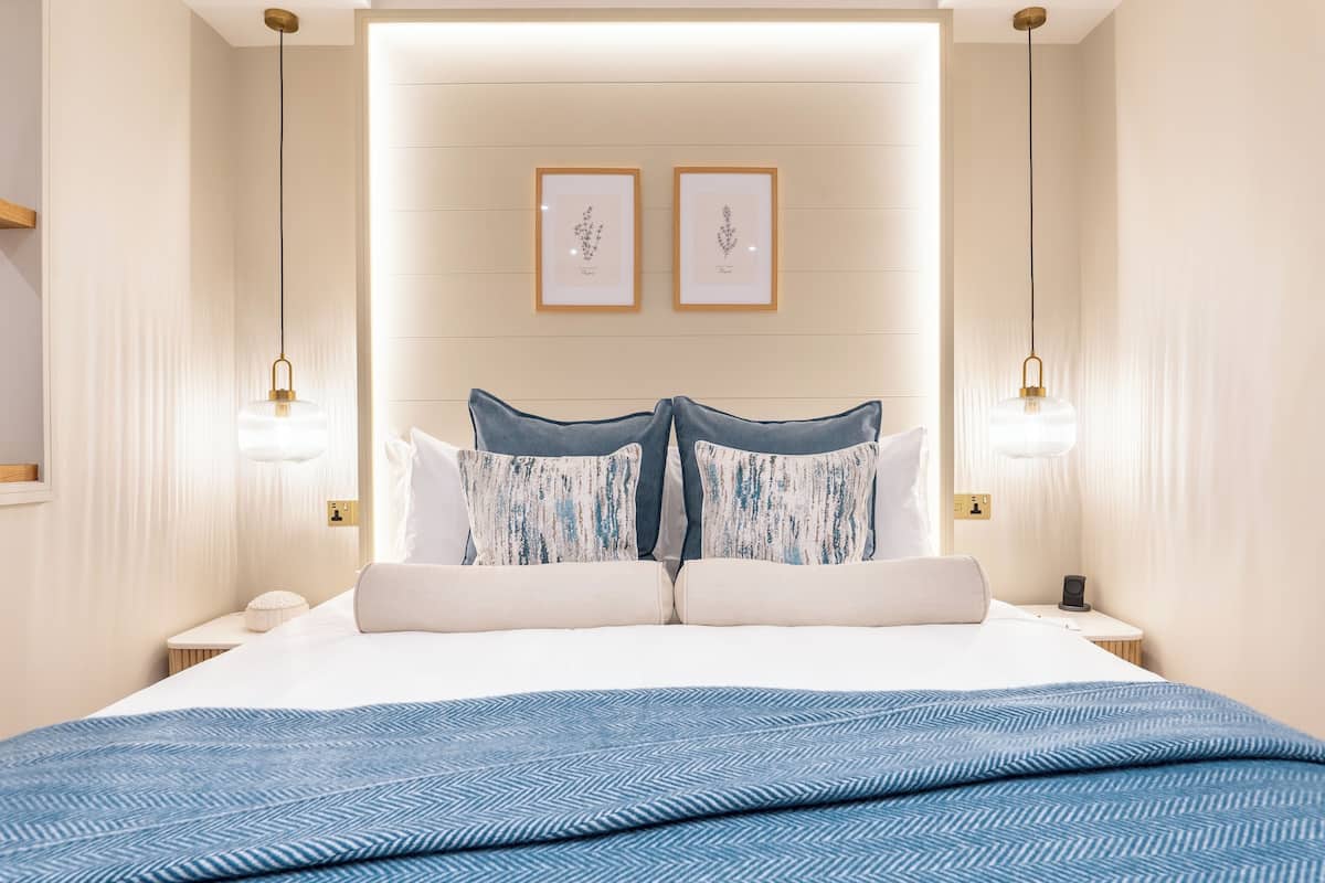 A neatly arranged bedroom with a large bed, two bedside tables, and framed botanical prints on the wall.