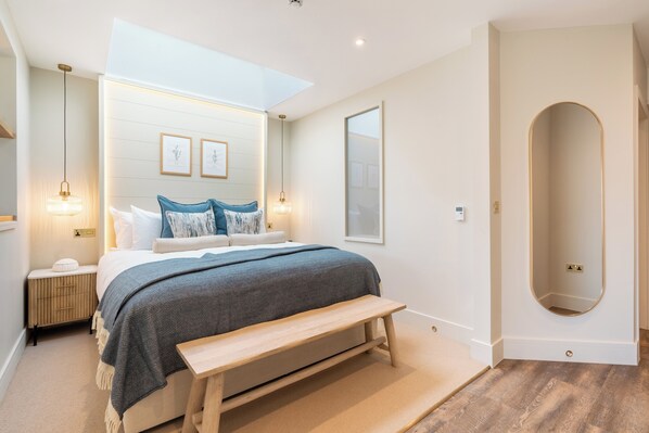 Un dormitorio moderno con una cama grande, un banco, un tragaluz y un espejo.