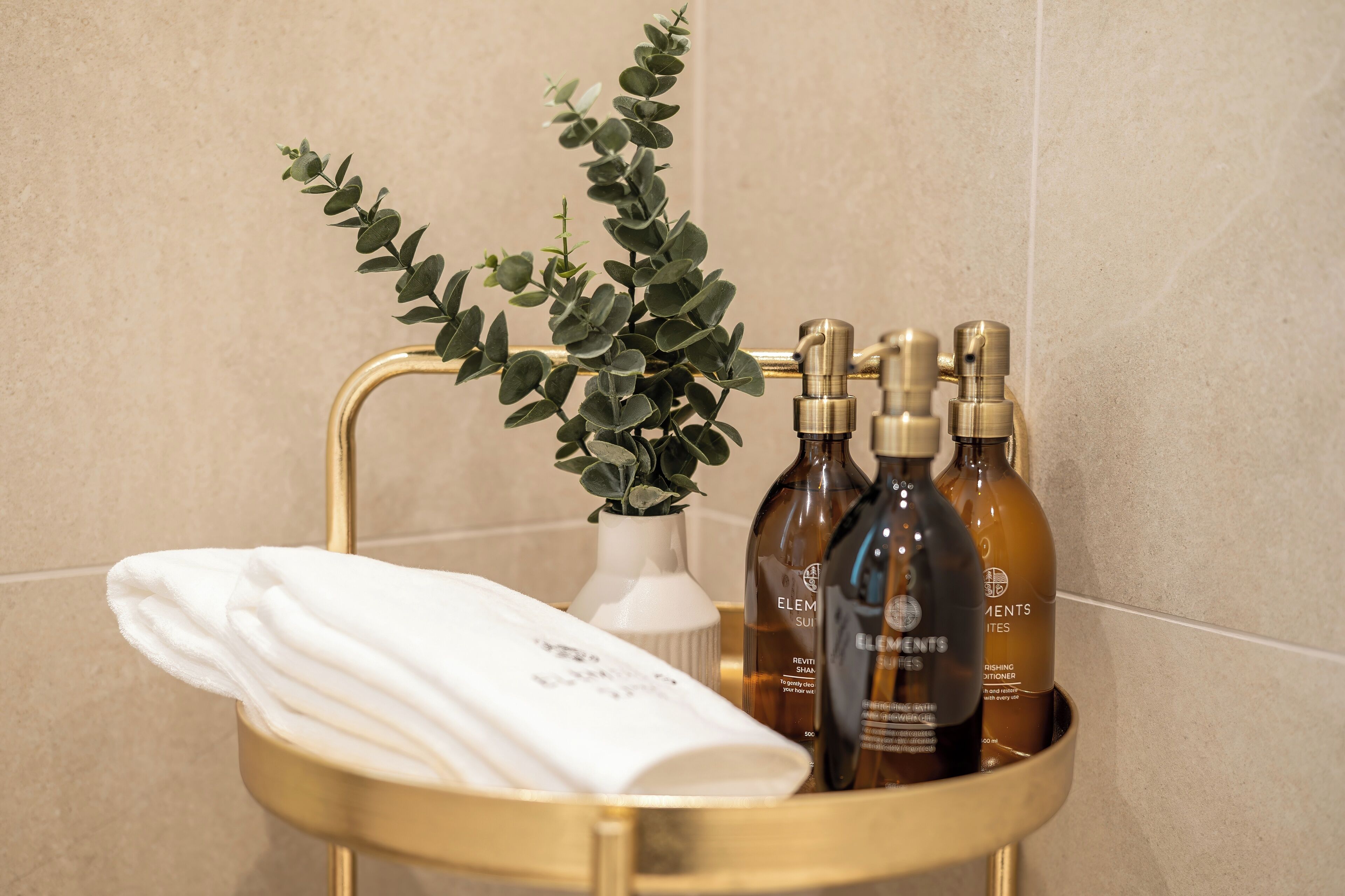 Un baño con tocador dorado, una toalla blanca y productos para el cuidado de la piel Elemis.