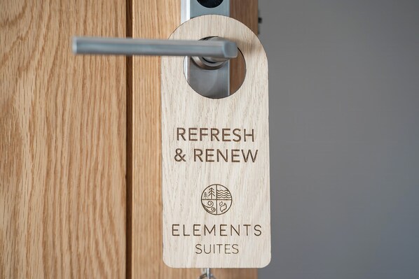 Una puerta de madera con un picaporte metálico y un letrero de madera que dice 'REFRESH & RENEW ELEMENTS SUITES'.