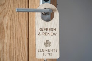 Una puerta de madera con un picaporte metálico y un letrero de madera que dice 'REFRESH & RENEW ELEMENTS SUITES'.