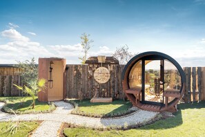Una estructura de madera rústica con un ventanal circular y una puerta, rodeada por una cerca de madera y un camino de grava.