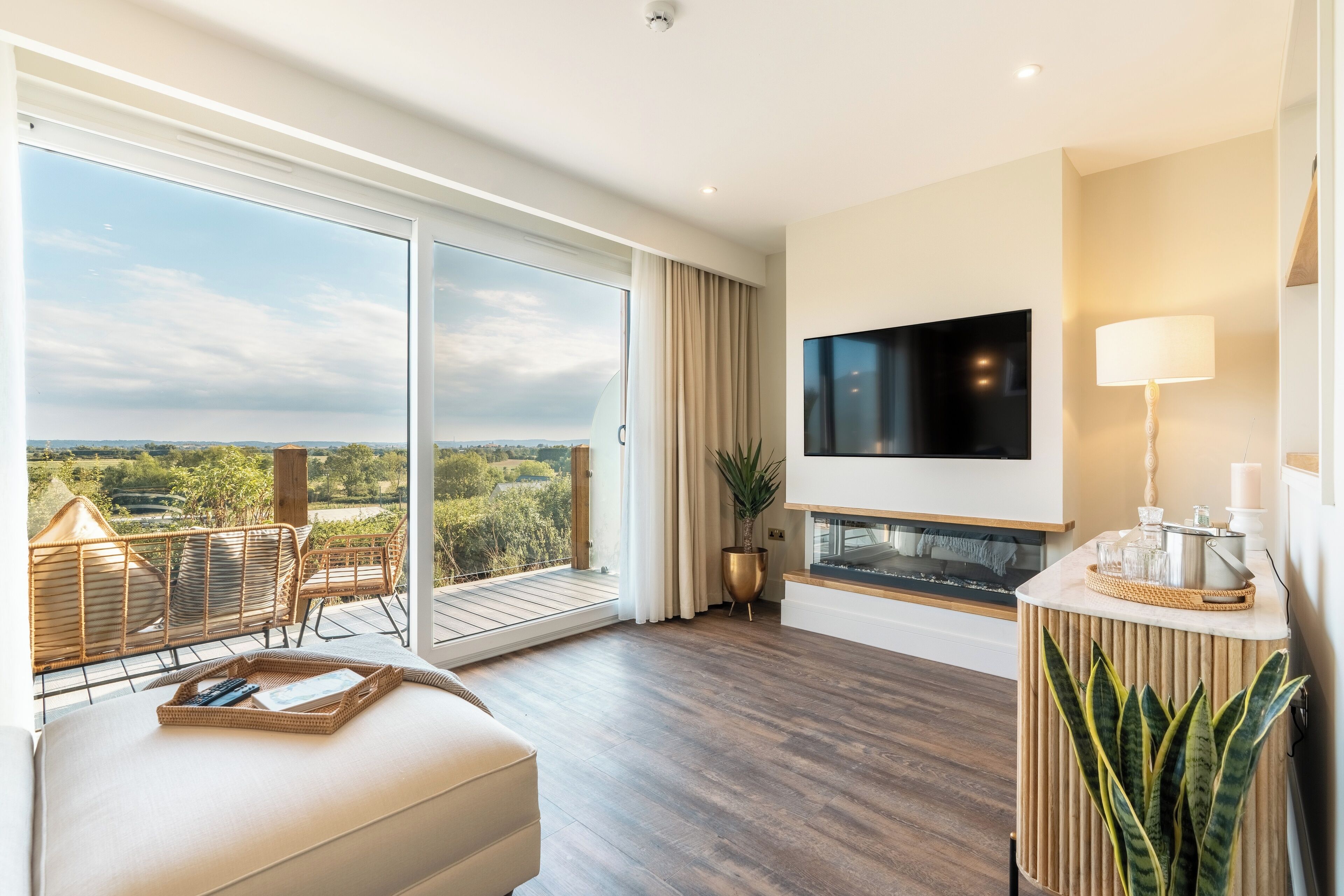 Un salón amplio con un televisor grande, una chimenea y un balcón con mobiliario de mimbre.