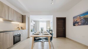 Una cocina moderna con zona de comedor, que presenta una mesa y sillas de madera, un horno empotrado y un cuadro en la pared.