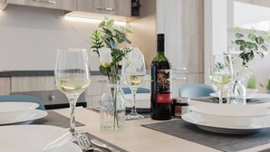 Una mesa de comedor con platos blancos, copas de vino y una botella de vino. Hay pequeños floreros de vidrio con flores y una botella de aceite de oliva sobre la mesa.