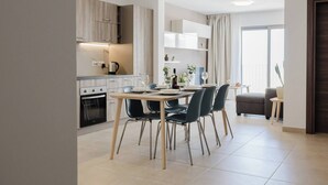 Una cocina moderna con comedor, que presenta una mesa preparada para cuatro personas, horno empotrado y un amplio ventanal con cortinas.