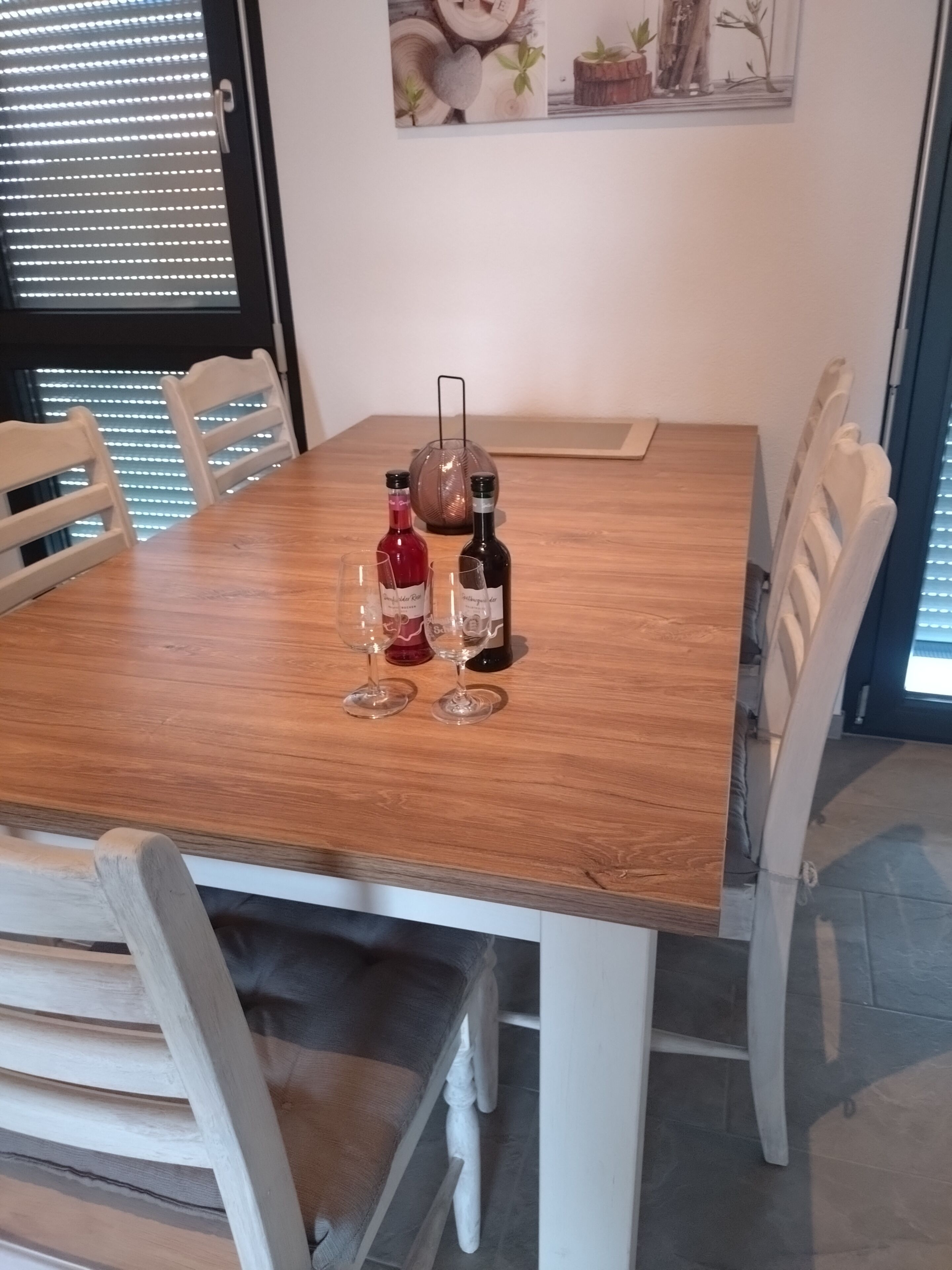 Un tavolo da pranzo con due bottiglie di vino e due bicchieri, circondato da sedie bianche.