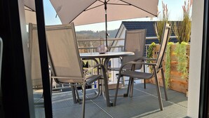 A patio with a table and chairs, a large umbrella, and a view of a house and trees. - Vacation apartment Bodensee-Suedwind sustainable maisonette with alpine view (Eigeltingen)