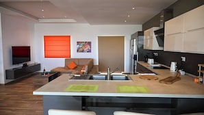 Una cocina moderna con una isla central, un comedor con sofá y un televisor en la sala de estar.