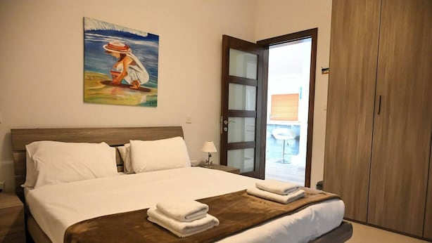 Habitación de hotel con una cama grande, un cuadro en la pared, un armario de madera y una puerta que da a un balcón.
