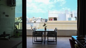 Un balcón con mesa y sillas, con vistas a un paisaje urbano de edificios y cielo despejado.