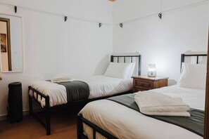 A room with two beds, a small wooden nightstand with a lamp, a trash bin, and a framed picture on the wall.