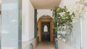 Un pasillo con suelo de baldosas, una puerta oscura al final y una planta a la derecha.